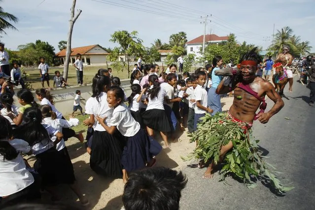 A local youth, front right, scares pupils on a street as he takes part in a ceremony to exorcize evil spirits and pray for rain amid the rice planting season at Pring Ka-ek village, northwest of Phnom Penh, Cambodia, Friday, May 22, 2015. Cambodia is a country which heavily relies on agriculture as over 80 percent of its 14 million people are farmers, growing rice as their main crop. (Photo by Heng Sinith/AP Photo)