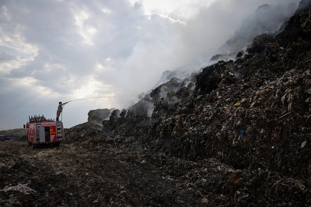 A firefighter works to douse fire as smoke billows from burning garbage at the Ghazipur landfill site in New Delhi, India on April 22, 2024. (Photo by Adnan Abidi/Reuters)