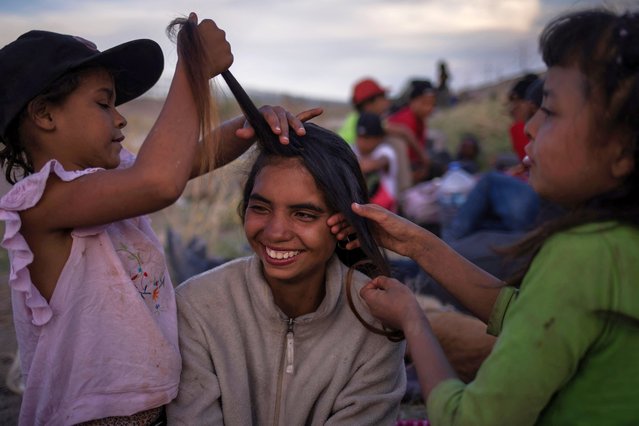 Haiseli, 7, of Venezuela, and compatriot Deimar, 9, brush the hair of their new friend Dayana, 15, of Colombia, as the migrants take rest along the dry riverbed of the Rio Grande while searching for an entry point into the United States from along the international boundary between Ciudad Juarez, Mexico and El Paso, Texas on April 24, 2024. (Photo by Adrees Latif/Reuters)
