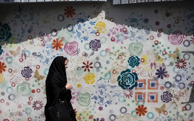 An Iranian woman walks past a graffiti in Tehran on May 15, 2017. After a series of bruising electoral defeats, Iranian conservatives campaigning in this week's presidential poll have belatedly embraced social media – a space long dominated by their reformist rivals. (Photo by Behrouz Mehri/AFP Photo)