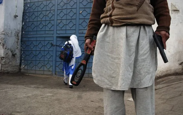 A man with a gun and a metal detector poses for photographers (unseen) while he stands outside a school after it reopened in Peshawar on January 12, 2015. Children streamed back to school across Pakistan on Monday in an anxious start to a new term following last month's massacre of 134 students at an army-run school in the volatile northwestern city of Peshawar. Most schools across the country of 180 million had been shut until Monday for an extended winter break in the aftermath of the Dec. 16 attack when Taliban militants broke into Army Public School and methodically killed the children. (Photo by Khuram Parvez/Reuters)