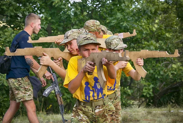 In this photo taken on Saturday, July 8, 2017, students at a paramilitary camp for children holding wooden mock-rifles with the trainer, left, with a real Kalashnikov rifle looking on outside Kiev, Ukraine. (Photo by Efrem Lukatsky/AP Photo)