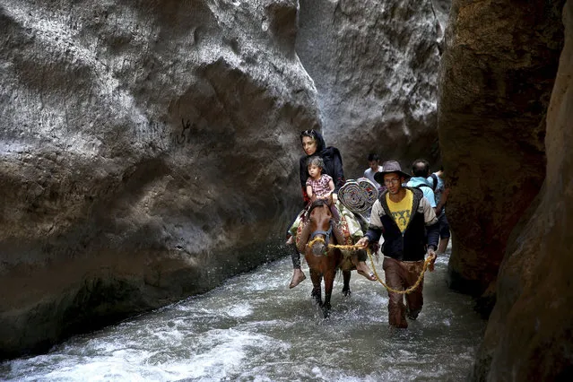 In this Monday, August 7, 2017, photo, a man leads his horse as two tourists ride in the river streaming between two cliffs at Tangeh Vashi canyon, just 99 miles (160 kilometers) north of Tehran, Iran. In a one-day excursion near the Iranian capital to escape the August heat in Tangeh Vashi, a canyon with an ice-cold mountain river streaming through, and a summer destination for many residents of the capital as well as neighboring provinces of Tehran. (Photo by Ebrahim Noroozi/AP Photo)