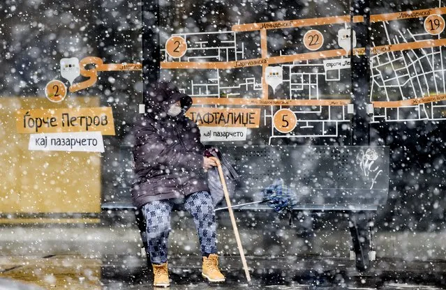 A woman wears a protective mask as she waits for public transport at a bus stop, during a heavy snowfall in Skopje on April 1, 2020. The coronavirus pandemic has claimed more than 30,000 lives in Europe alone, a global tally showed on April 1, 2020, in what the head of the United Nations has described as humanity's worst crisis since World War II. (Photo by Robert Atanasovski/AFP Photo)