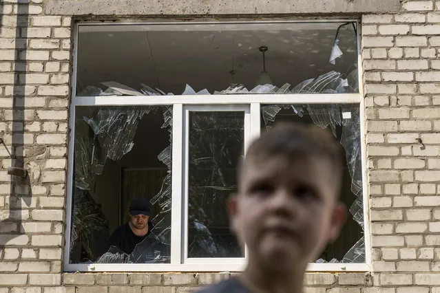 A worker cleans up inside as Tikhon Pavlov, 11, walks past the Kramatorsk College of Technologies and Design, where he used to take karate lessons, after an early morning rocket attack in Kramatorsk, Donetsk region, eastern Ukraine, Friday, August 19, 2022. Russia continued to shell towns and villages in Ukraine's embattled eastern Donetsk region, according to regional authorities, where Russian forces are pushing to overtake areas still held by Ukraine. (Photo by David Goldman/AP Photo)