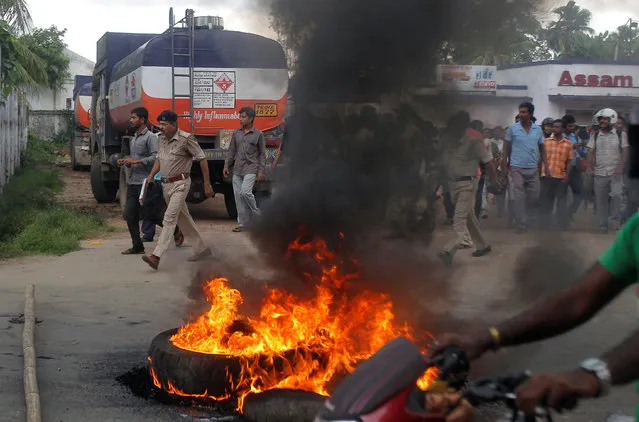 A police officer (2nd L) walks past burning tyres set on fire by demonstrators protesting against petrol crisis caused by damaged section of the Assam-Tripura national highway after incessant rains, in Agartala, India, July 29, 2016. (Photo by Jayanta Dey/Reuters)