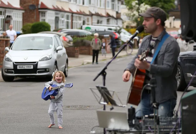 A young girl holds a guitar as musician Aaron performs for local residents, following the outbreak of the coronavirus disease (COVID-19), Enfield, Britain, May 3, 2020. (Photo by Tom Jacobs/Reuters)