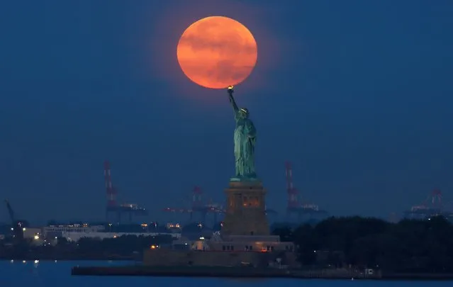 The full Harvest Moon sets behind the Statue of Liberty as the sun rises on September 10, 2022, in New York City. (Photo by Gary Hershorn/Getty Images)