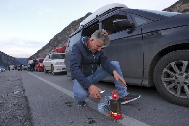 A man gets ready to cook next to his car, with other cars queuing to the border between Georgia and Russia at Verkhny Lars, as they leave Chmi, North Ossetia–Alania Republic, Russia, Wednesday, September 28, 2022. Long lines of vehicles have formed at a border crossing between Russia's North Ossetia region and Georgia after Moscow announced a partial military mobilization. (Photo by AP Photo/Stringer)