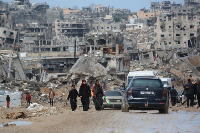 Displaced Palestinians walk through a muddy road amid the destruction in Jabalia in the northern Gaza Strip on February 6, 2025, during a truce in the war between Israel and Hamas. In hunger-stricken makeshift shelters set up in former schools, bombed-out houses and cemeteries across the Gaza Strip, devastated by 15 months of war between Hamas and Israel, hundreds of thousands lack even plastic sheeting to protect from winter rains and biting winds, aid workers say. (Photo by Bashar Taleb/AFP Photo)