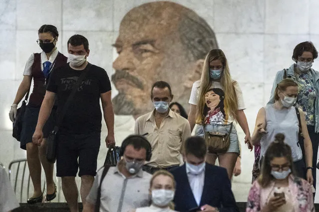 People wearing face masks to protect against coronavirus walk through the subway, with a portrait of Soviet founder Vladimir Lenin in the background, in Moscow, Russia, Wednesday, June 10, 2020. Moscow residents are no longer required to stay at home or obtain electronic passes for traveling around the city. All restrictions on taking walks, using public transportation or driving have been lifted as well. (Photo by Pavel Golovkin/AP Photo)