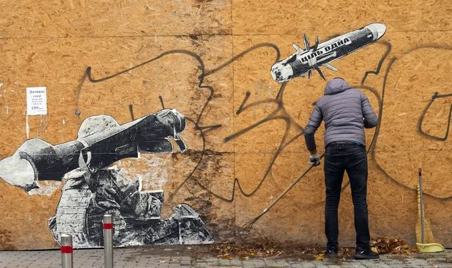 A street cleaner sweeps the autumn leaves near graffiti depicting a Ukrainian soldier firing an anti-tank missile in Kyiv, Ukraine, Monday, October 24, 2022. Writing on the missile reads: “The goal is one”. Eight months ago, on Feb. 24, Russia launched an invasion of Ukraine. (Photo by Efrem Lukatsky/AP Photo)