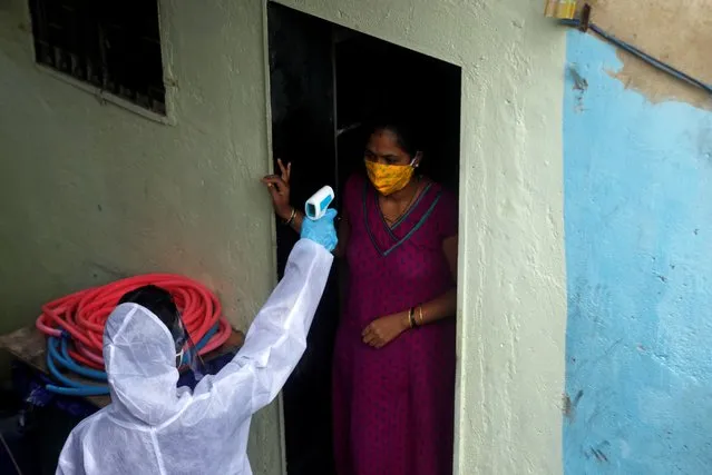 A healthcare worker wearing personal protective equipment (PPE) checks the temperature of a resident of a slum area during a check-up camp for the coronavirus disease (COVID-19) in Mumbai, India June 27, 2020. (Photo by Francis Mascarenhas/Reuters)