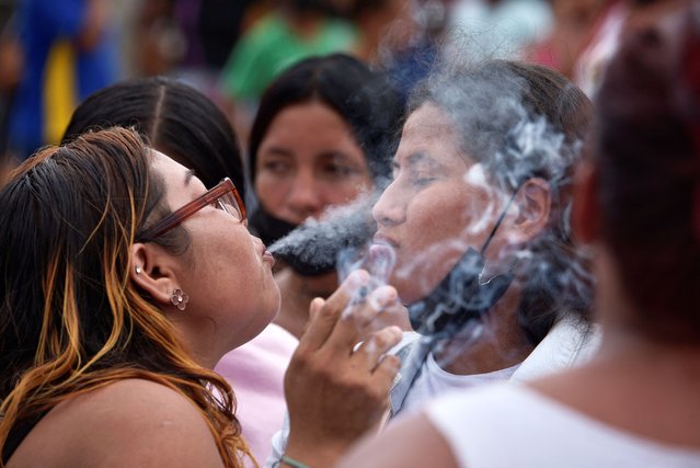 A woman blows cigarette smoke at another woman in the belief that this will help alleviate the effects of tear gas fired by police officers, during a protest to demand fair treatment of their loved ones, outside the Litoral prison in Guayaquil, Ecuador, on January 22, 2024. (Photo by Vicente Gaibor del Pino/Reuters)
