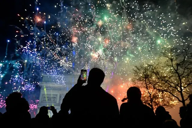 A spectator holds a smartphone as fireworks explode next to the Arc de Triomphe, at the Avenue des Champs-Elysees during New Year celebrations in Paris, early on January 1, 2023. (Photo by Julien De Rosa/AFP Photo)