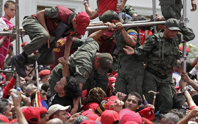 Servicemen help a woman move out of the crowd waiting to see the body of Venezuela's late President Hugo Chavez at the military academy where he is lying in state in Caracas, Venezuela, Thursday, March 7, 2013. While Venezuela remains deeply divided over the country's future, the multitudes who reached the president's coffin early Thursday were united in grief and admiration for a man many considered a father figure.  (Photo by Ariana Cubillos/AP Photo)
