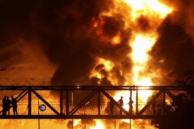 People watch from a bridge as flames from an Israeli attack rise from Sharan Oil depot, following Israeli strikes on Iran, in Tehran, Iran, on June 15, 2025. (Photo by Majid Asgaripour/WANA (West Asia News Agency) via Reuters)
