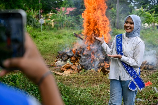 A woman poses for photographs while Indonesian police officers burn seized various drugs during a press conference at the regional police headquarters in Banda Aceh on June 12, 2025. (Photo by Chaideer Mahyuddin/AFP Photo)