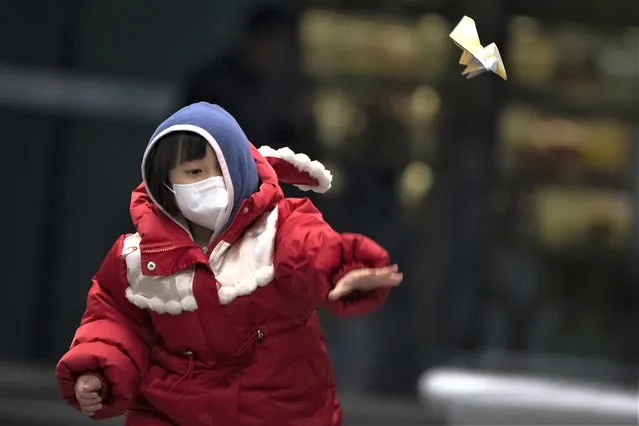 A boy wearing a face mask throws a paper airplane as he plays at a shopping and office complex in Beijing, Thursday, February 9, 2023. (Photo by Mark Schiefelbein/AP Photo)