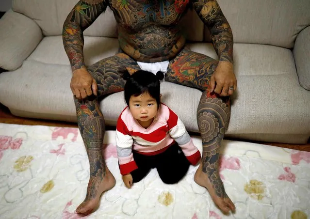 Scrap yard worker Hiroyuki Nemoto, 48, poses for a photo with his 1-year-old daughter Tsumugi at their home in Hitachinaka, Ibaraki Prefecture, Japan on January 10, 2020. A proud, growing tribe of Japanese ink aficionados are defying deeply-rooted taboos associating tattoos with crime, turning their skin into vivid palettes of color with elaborate full-body designs. (Photo by Kim Kyung-Hoon/Reuters)