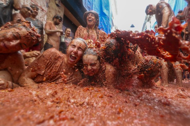 Revellers lie in a pool of squashed tomatoes during the annual “Tomatina” tomato fight fiesta, in the village of Bunol near Valencia, Spain, Wednesday, August 28, 2024. (Photo by Alberto Saiz/AP Photo)