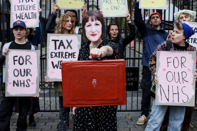 A demonstrator holds a mock red budget box while wearing a mask representing Britain's Chancellor of the Exchequer Rachel Reeves, during a protest outside Downing Street in London, Britain on October 30, 2024. (Photo by Isabel Infantes/Reuters)
