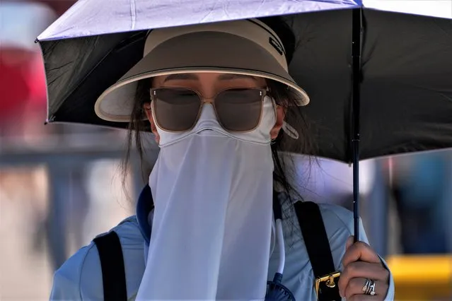 A woman wear a face cover and carry an umbrella to shield from the sun as she walks on a street on a hot day in Beijing, Thursday, June 29, 2023. (Photo by Andy Wong/AP Photo)