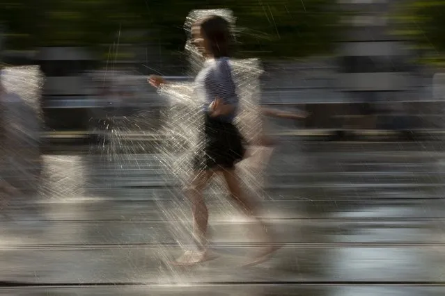 A girl cools herself running through a fountain at a park in Moscow, Russia, Friday, Aug. 3, 2018. The hot weather in Moscow is continuing, with temperatures forecast to reach 30 degrees Celsius (86 Fahrenheit). (Photo by Alexander Zemlianichenko/AP Photo)