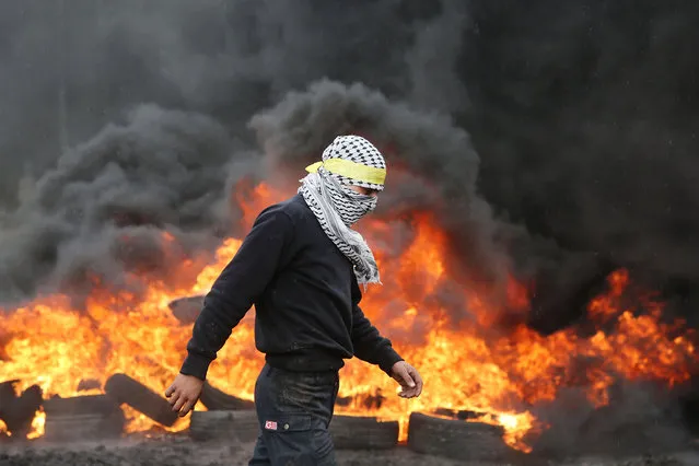 A Palestinian protester walks past burning tyres during clashes with Israeli security forces following a demonstration against the expropriation of Palestinian land by Israel, on January 8, 2016, in the village of Kafr Qaddum, near the city of Nablus in the Israeli occupied West Bank. (Photo by Jaafar Ashtiyeh/AFP Photo)