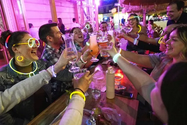 Emily Baumgartner, left, and Luke Finley, second from left, join friends from their church group in a birthday toast to one of the members, upper right, during their weekly “Monday Night Hang” gathering at the Tiki Bar on Manhattan's Upper West Side Monday, May 17, 2021, in New York. “Most of us live alone. and we need community. During the pandemic, we started hanging out in the park (Central Park) once a week. Once bars and restaurants reopened, we started coming back to Tiki Bar afterward. Under the latest regulations, vaccinated New Yorkers can shed their masks in most situations Wednesday. Restaurants, shops, gyms and many other businesses can go back to full occupancy if all patrons are inoculated”. (Photo by Kathy Willens/AP Photo)
