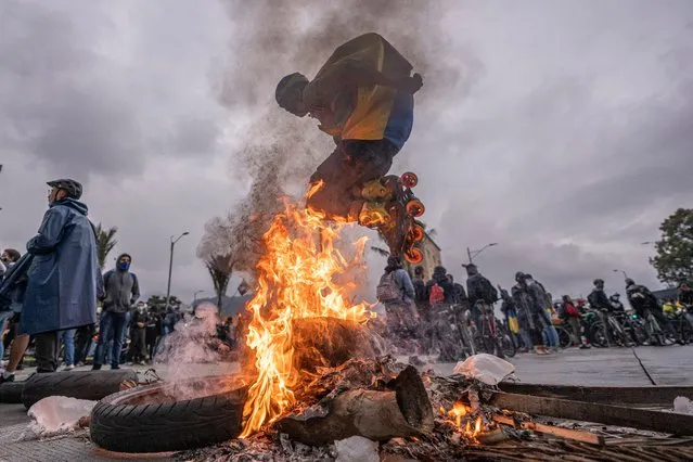 A demonstrator in roller skates wearing a Colombian flag on his back jumps over a bonfire during national strike on May 5, 2021 in Bogota, Colombia. Despite that the ruling party announced withdrawal of the unpopular bill for a tax reform and the resignation of the Minister of Finances, social unrest continues after a week. The United Nations human rights office (OHCHR) showed its concern and condemned the riot police repression. Ongoing protests take place in major cities since April 28. (Photo by Diego Cuevas/Getty Images)