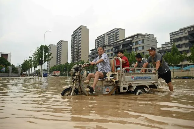 People wade through a flooded street following a heavy rain in Zhengzhou, in China's Henan province on July 22, 2021. (Photo by Noel Celis/AFP Photo)