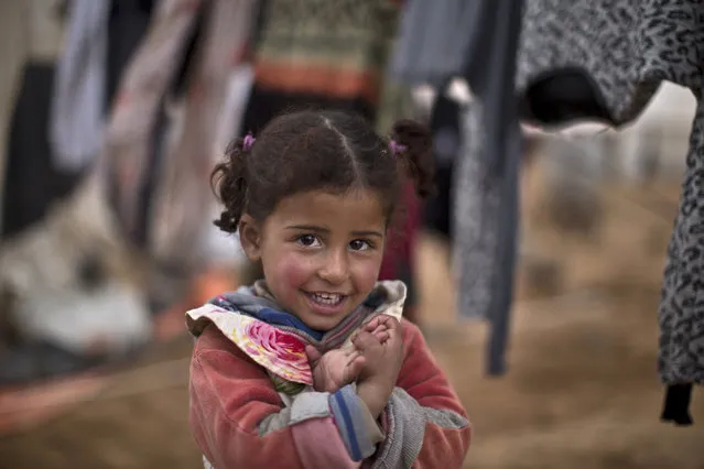 In this Wednesday, January 20, 2016, file photo, Syrian refugee Bissan Alabdullah, almost 3, smiles while standing next to her family's laundry outside their tent at an informal tented settlement near the Syrian border on the outskirts of Mafraq, Jordan. (Photo by Muhammed Muheisen/AP Photo)