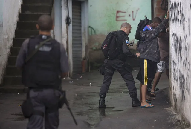 A police officer searches residents in a alley of the Alemao slum complex as part of a security reinforcement by the UPP (Police Pacification Unit) in Rio de Janeiro, Brazil, Tuesday, April 7, 2015. Authorities have reinforced the area due to the violence that has wracked the Complexo Alemao in recent days, with a young boy and a 41-year-old housewife killed by stray bullets as gangs and police exchange intense gunfire. (Photo by Leo Correa/AP Photo)