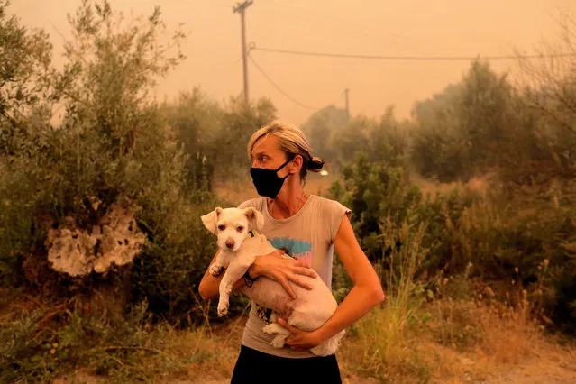 A local resident holds her dog that was rescued by locals during a wildfire at the village of Pefki in the Evia, Greece, 08 August 2021. Fires that broke out in Attica and Evia island this week have burned more than a quarter of a million stremmas, the National Observatory of Athens' center Beyond said on 08 August. Some 76,150 stremmas (7,615 hectares) have been burnt so far in northern Attica. At Evia island the surface area of burnt land is measured at 197,940 stremmas (19,794 hectares). These figures concern only the fires in Attica and Evia, but dozens of large fires have affected several areas across the country. (Photo by Kostas Tsironis/EPA/EFE)