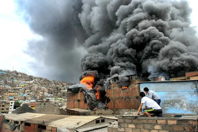 People observe as a fire ravages through a tire wharehouse in downtown Lima on December 10, 2013. The toxic smoke from the tires left at least 2 firefighters and 14 civilians injured. (Photo by AFP Photo/STR)