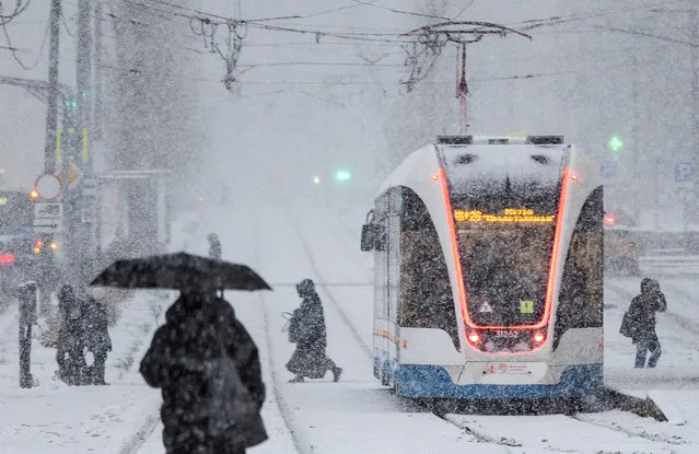People cross a tram lane during a snowfall on the first snowy day of the season, in Moscow, Russia on October 27, 2023. (Photo by Maxim Shemetov/Reuters)