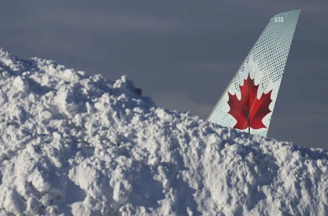 The tail of an Air Canada aircraft is seen behind a pile of snow at Vancouver International Airport in Richmond, British Columbia, Wednesday, December 21, 2022. The airport is limiting international flights to carriers registered in Canada and the U.S. for two days as it attempts to clear a backlog of aircraft and passengers after a snowstorm caused massive disruptions this week. (Photo by Darryl Dyck/The Canadian Press via AP Photo)