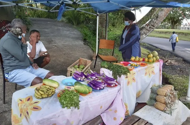 A family sells produce in front of their home in Suva, Fiji, Thursday, June 24, 2021. Mosese Soro, left, had to give up his business buying and selling fish because it can't operate while Fiji's borders are closed due to COVID restrictions. (Photo by Aileen Torres-Bennett/AP Photo)