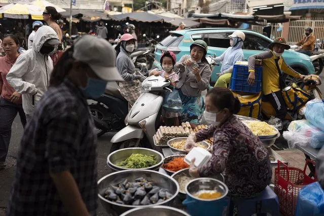 A shopper sitting on a scooter counts money after buying food from a street vendor in Ho Chi Minh City, Vietnam, January 11, 2024. (Photo by Jae C. Hong/AP Photo)