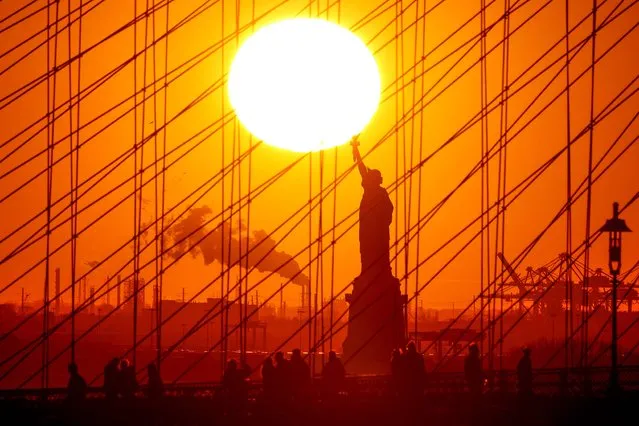 The sun sets behind the Statue of Liberty as people walk on the Brooklyn bridge in New York on February 6, 2024. (Photo by Charly Triballeau/AFP Photo)