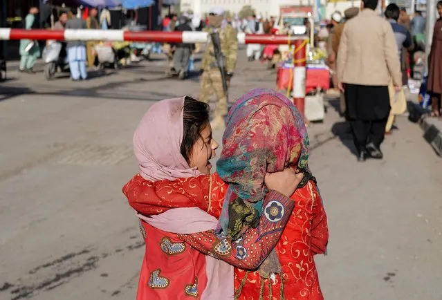 Girls cuddle each other as they walk near a Taliban fighter at a market in Kabul, Afghanistan on October 24, 2021. (Photo by Zohra Bensemra/Reuters)