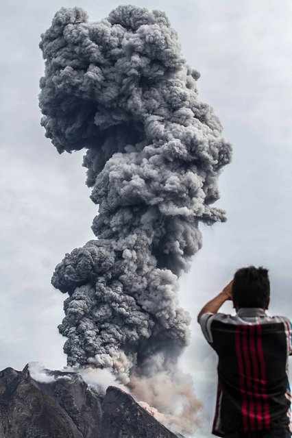 A villager takes a photograph as Mount Sinabung volcano spews thick volcanic ash, as seen from Beganding village in Karo, North Sumatra province, on May 19, 2017. Sinabung roared back to life in 2010 for the first time in 400 years. After another period of inactivity, it erupted once more in 2013 and has remained highly active since. (Photo by Ivan Damanik/AFP Photo)