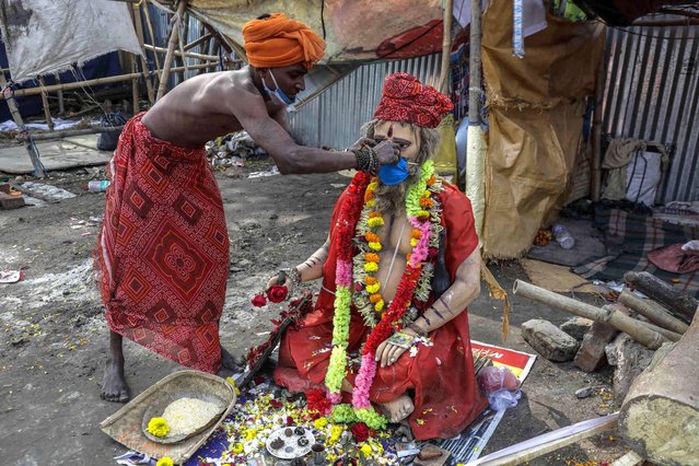 A Hindu holy man not wearing his mask properly adjusts a face mask on a clay image of a holy man at the transit camp prior to the Makar Sangkranti holy dip in Kolkata, India, Thursday, January 13, 2022. The auspicious holy dip is scheduled on Jan. 14. (Photo by Bikas Das/AP Photo)