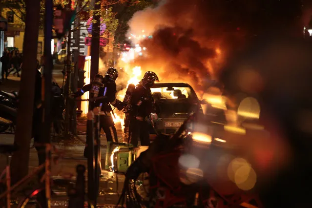 Firefighters extinguish a burning car as French Gendarmerie clear the Place de la Republique in Paris during a protest by the Nuit Debout, or “Up All Night” movement who have been rallying against the French government's proposed labour reforms early on April 29, 2016. Twenty-seven people were arrested and 24 detained during the overnight clashes in the French capital as the police dispersed the protesters who movement began on March 31 in opposition to the government's proposed labour reforms. (Photo by Joel Saget/AFP Photo)