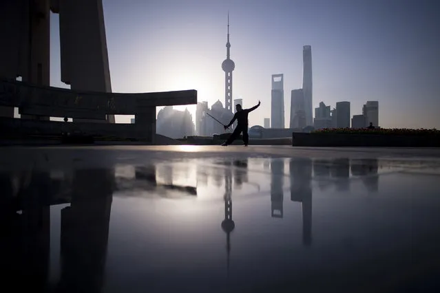 A man practice Tai Chi with a sword  during sunrise at the promenade on the Bund along the Huangpu River, seen against the skyline of the Lujiazui Financial District in Pudong, Shanghai  March 17, 2017. (Photo by Johannes Eisele/AFP Photo)