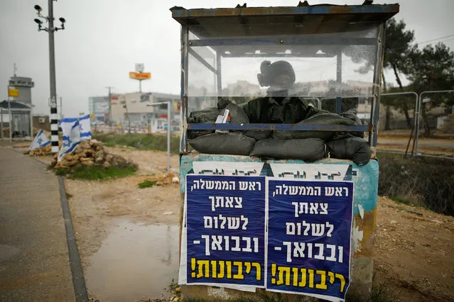 An Israeli soldier stands inside a guarding booth covered in posters with texts in Hebrew reading “Prime Minister, we bid you farewell and upon your return – sovereignty!” at a junction in the Gush Etzion Israeli settlement block in the occupied West Bank February 15, 2017. (Photo by Amir Cohen/Reuters)