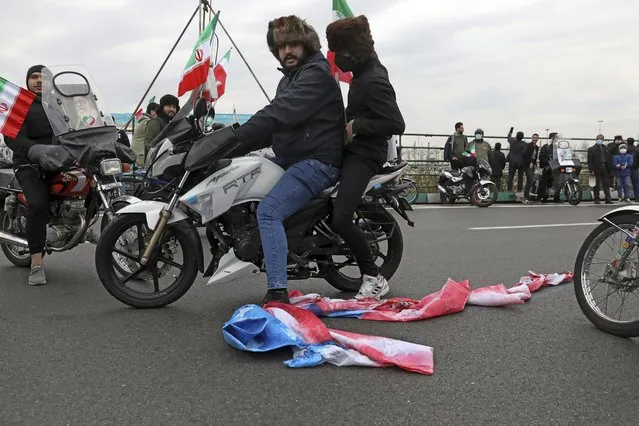 A man on a motorcycle pulls a burnt representation of the U.S. flag on the ground during the annual rally commemorating the anniversary of1979 Islamic Revolution in Tehran, Iran, Friday, February 11, 2022. Thousands of cars and motorbikes paraded in the celebration, although fewer pedestrians were out for a second straight year due to concerns over the coronavirus pandemic. (Photo by Vahid Salemi/AP Photo)