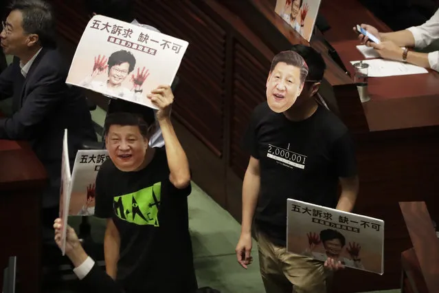 Pan-democratic legislators wearing masks of Chinese President Xi Jinping protest as Hong Kong Chief Executive Carrie Lam attempts to give a policy speech at the Legislative Council in Hong Kong, Wednesday, October 16, 2019. In chaotic scenes, furious pro-democracy lawmakers twice forced Hong Kong's leader to stop delivering a speech laying out her policy objectives and clamored for her to resign after she walked out of the legislature on Wednesday and then delivered the annual address 75 minutes late via television. (Photo by Mark Schiefelbein/AP Photo)