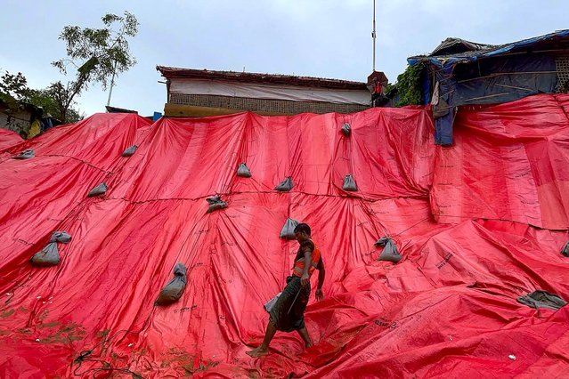 A Rohingya volunteer covers a landslide affected area with tarpaulin at the Balukhali refugee camp in Ukhia at Bangladesh's Cox's Bazar on June 19, 2024. Torrential rains in Bangladesh have triggered landslides burying alive at least nine people and forcing thousands to flee to higher ground, police and government officials in the low-lying nation said on June 19. (Photo by AFP Photo)